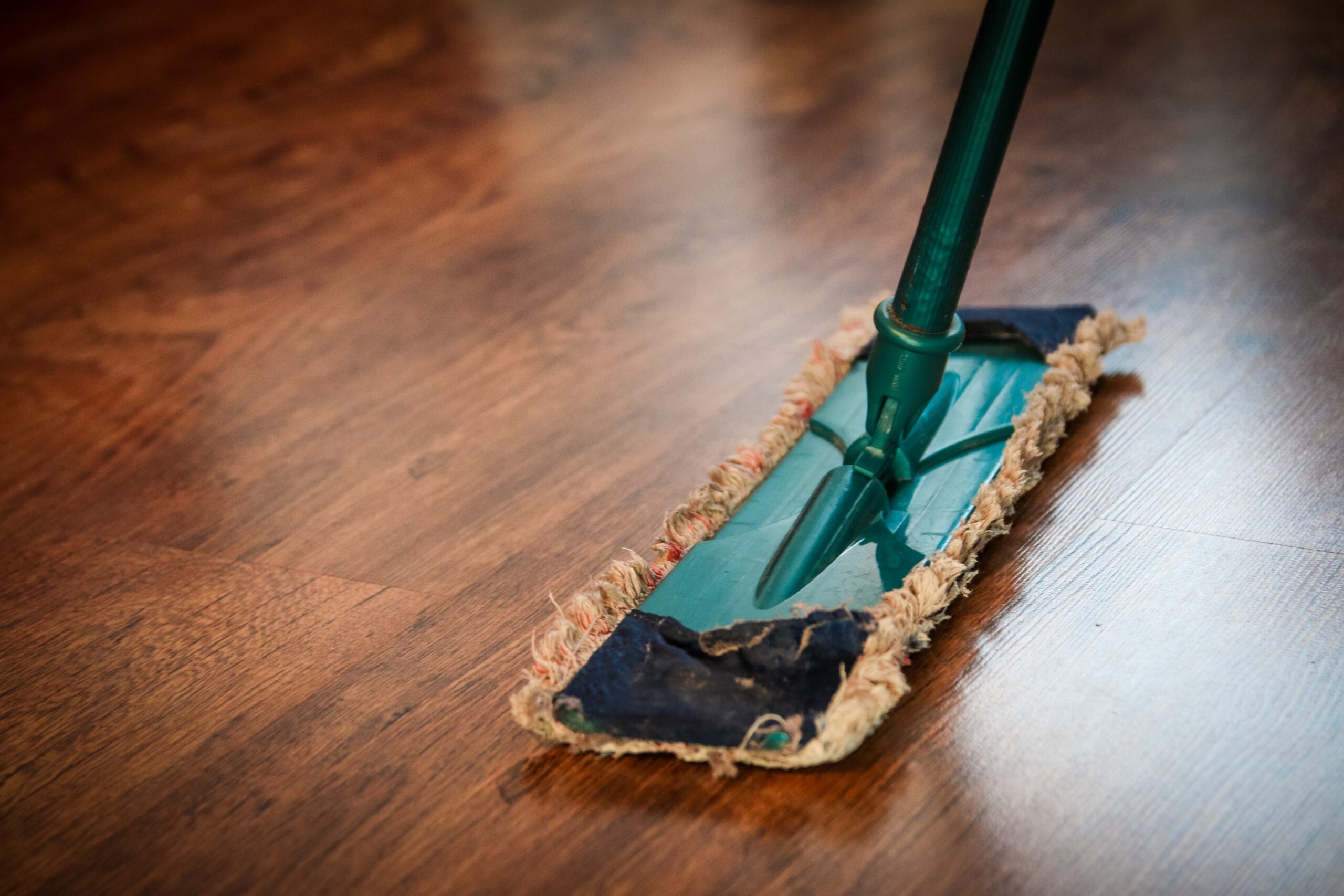 is-it-time-to-consider-assisted-living mop with a brown pad and green handle standing upright on a brown, wooden floor