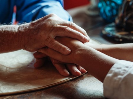 older male wearing a blue shirt holding the hands on a young, female adult wearing a white shirt