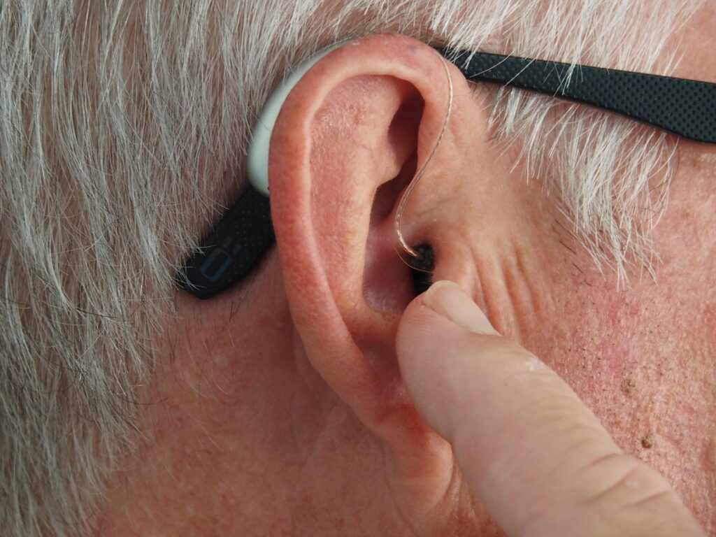 person with short gray hair and dark-framed glasses inserting a hearing aid