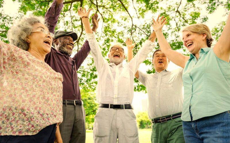 seniors standing in a semi-circle with their arms raise and smiles on their faces; trees in the background