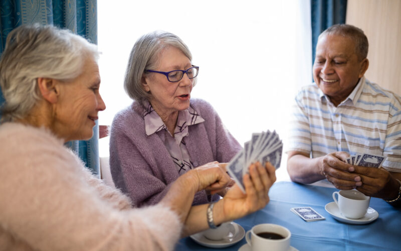 Smiling senior woman showing cards to friends while playing at table in nursing home
