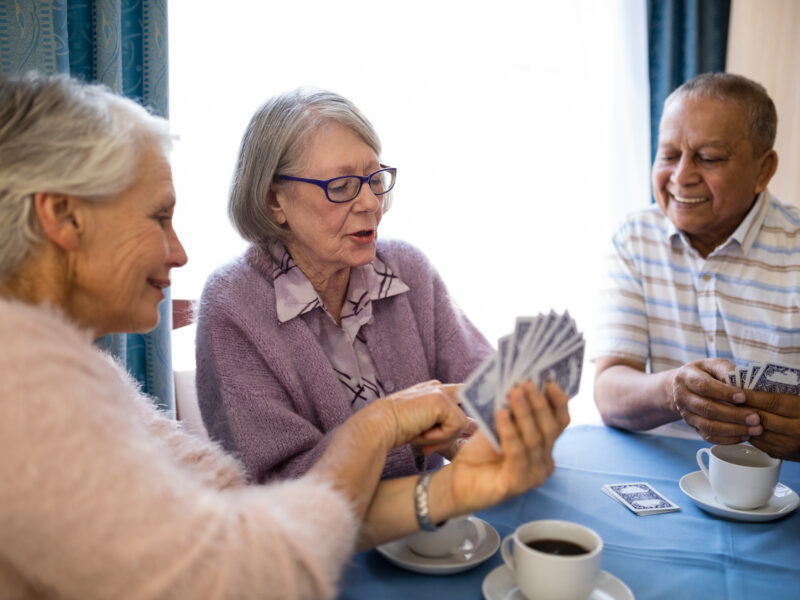 Smiling senior woman showing cards to friends while playing at table in nursing home