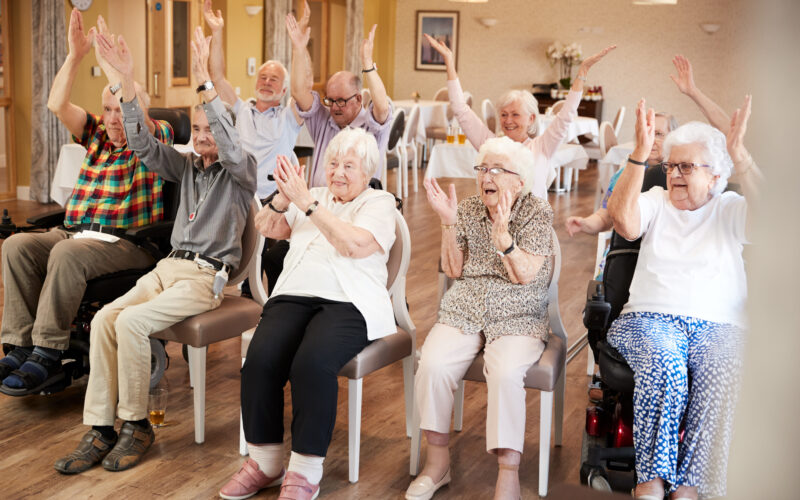 Carer Leading Group Of Seniors In Fitness Class In Retirement Home