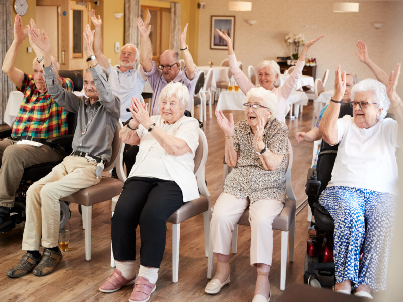 Carer Leading Group Of Seniors In Fitness Class In Retirement Home