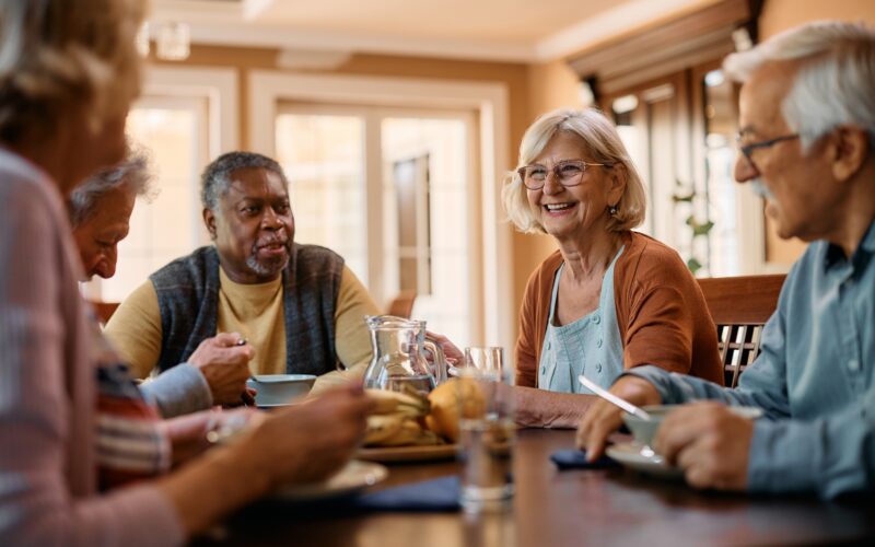 group of seniors at a table smiling and communicating while eating a meal together