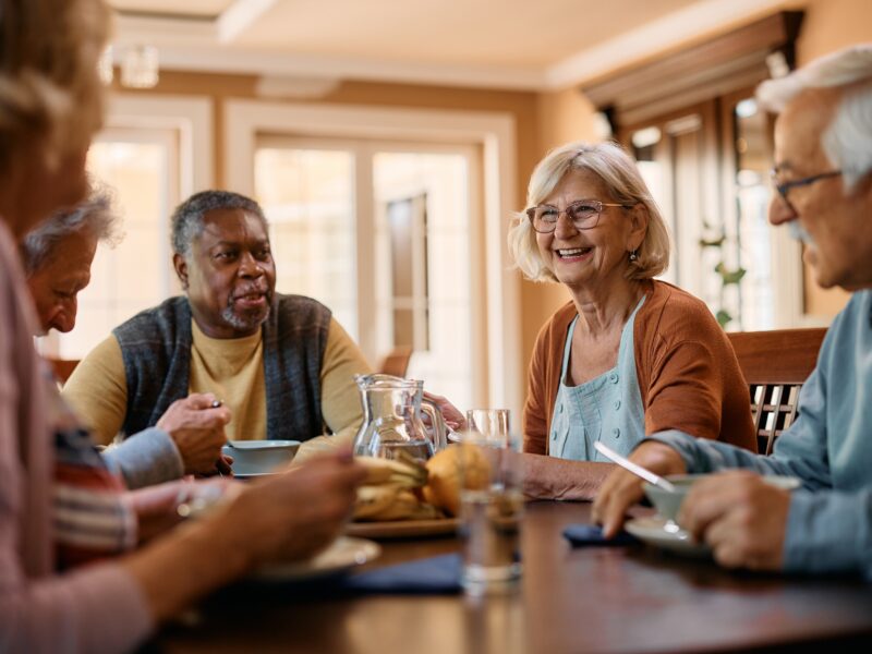 group of seniors at a table smiling and communicating while eating a meal together